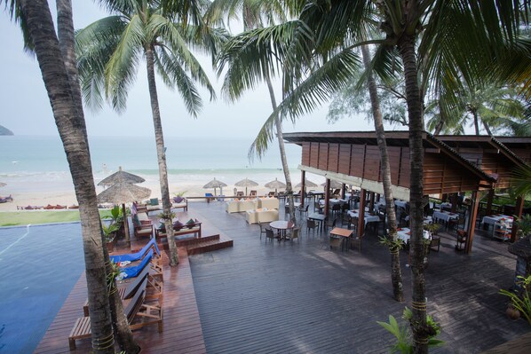 A beachside resort with outdoor seating, palm trees, and a view of the ocean.