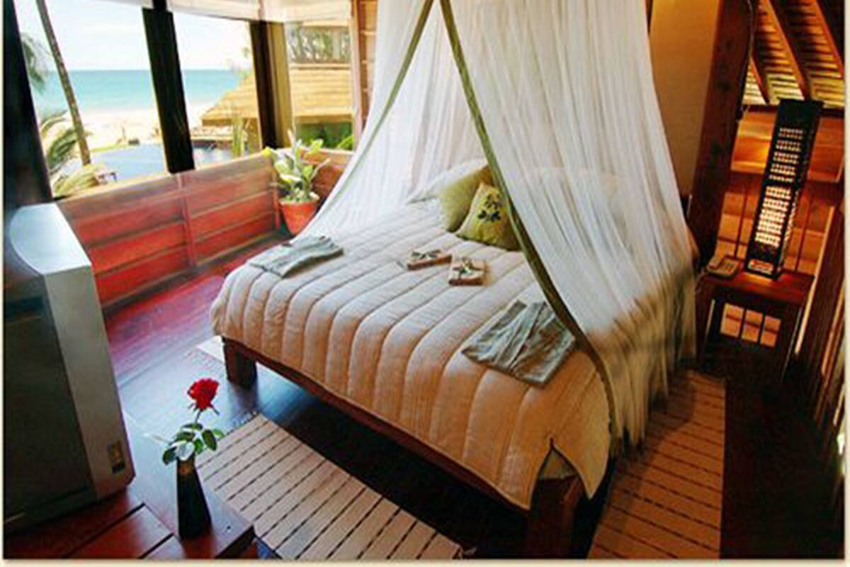 A bedroom with a bed, a nightstand, a potted plant, and a view of the beach.