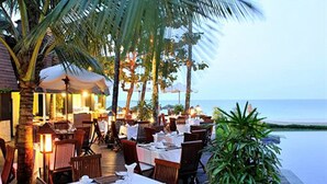 An outdoor dining area with tables set for two, surrounded by palm trees and overlooking the ocean. - Amata Resort & Spa (Ngapali)