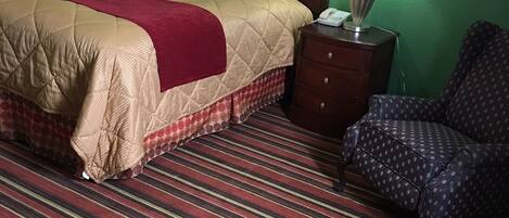 A hotel room with a bed, a nightstand, a chair, and a striped carpet.