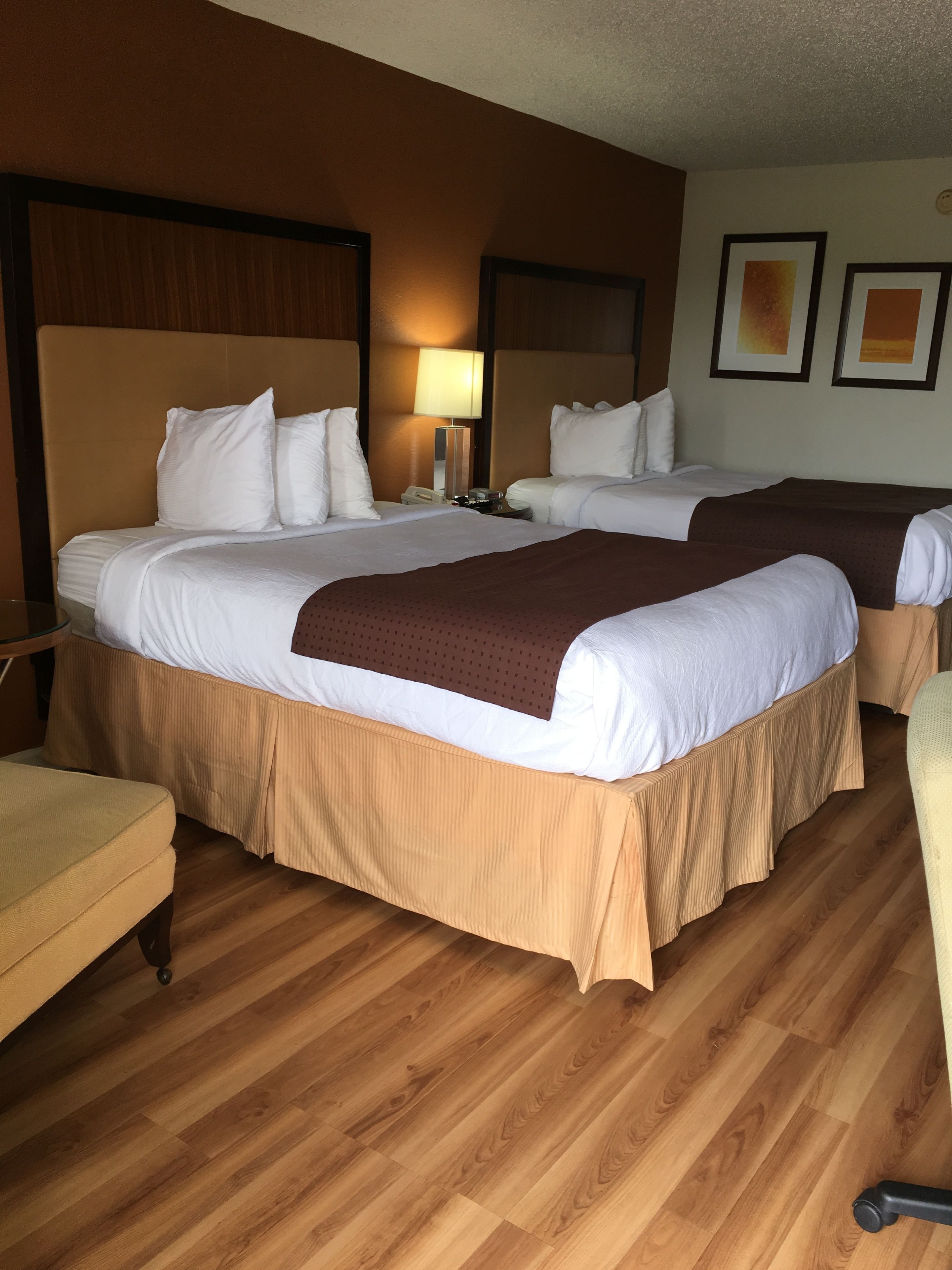 Een hotelkamer met twee bedden, een nachtkastje met een lamp, een stoel en houten vloeren.