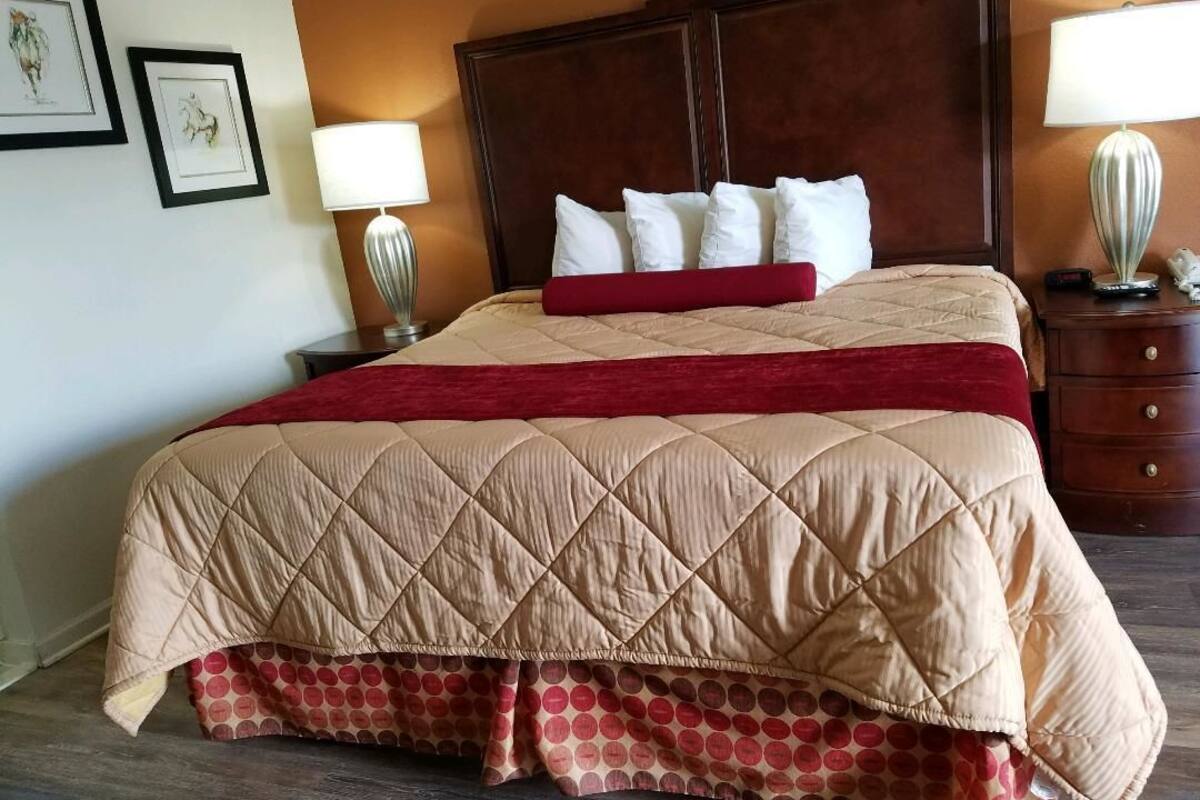 Quarto de hotel com uma cama grande, cabeceira de madeira, duas mesas de cabeceira com abajures e quadros nas paredes.