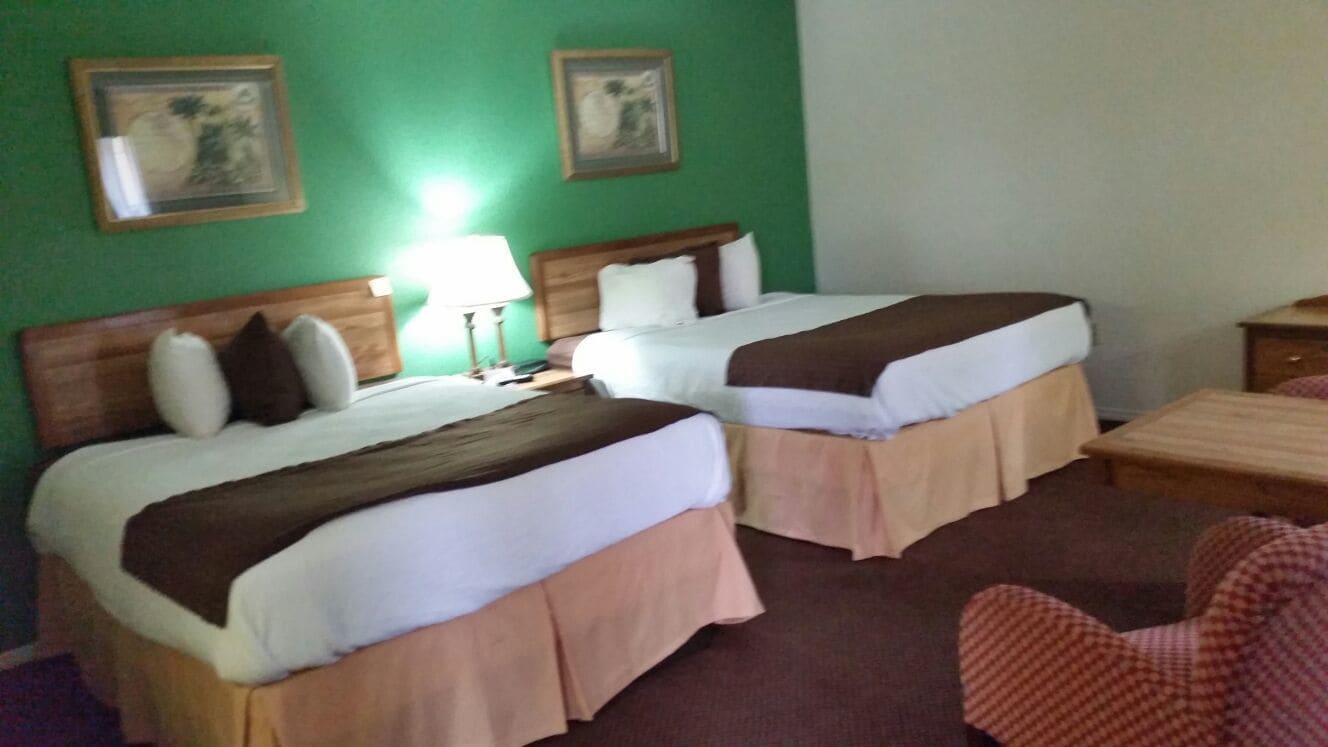 Ein Hotelzimmer mit zwei Betten, einem Holzkopfende, einem Nachttisch mit Lampe und einem Sessel.