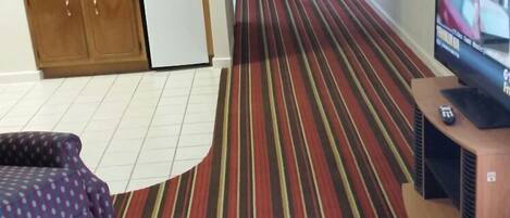 A room with a striped carpet, a television, and a kitchenette.