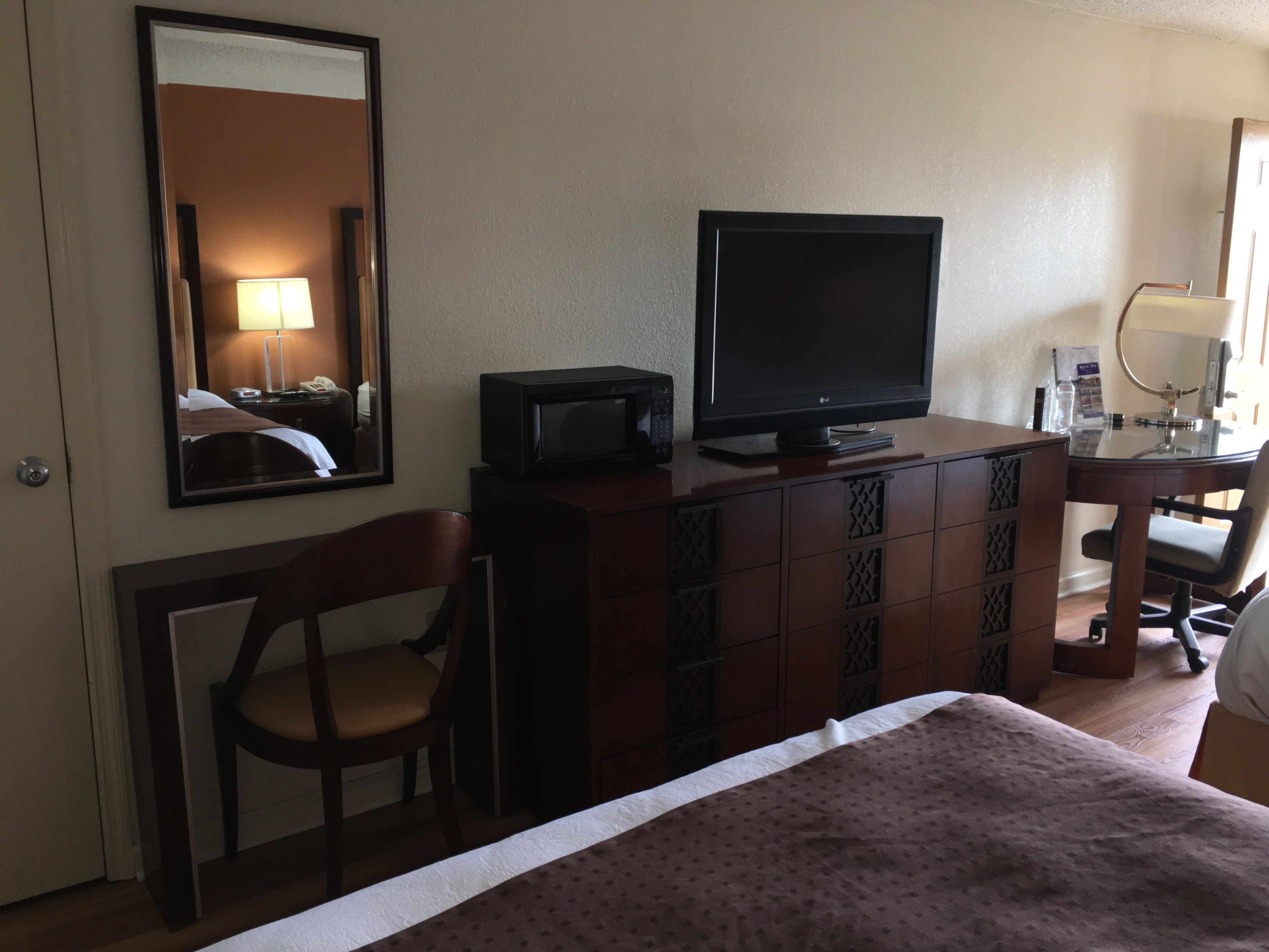 Een hotelkamer met een bed, een bureau met een computer en beeldscherm, een stoel, een dressoir en een spiegel.
