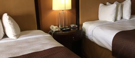 A hotel room with two beds, a nightstand with a lamp, and a telephone.