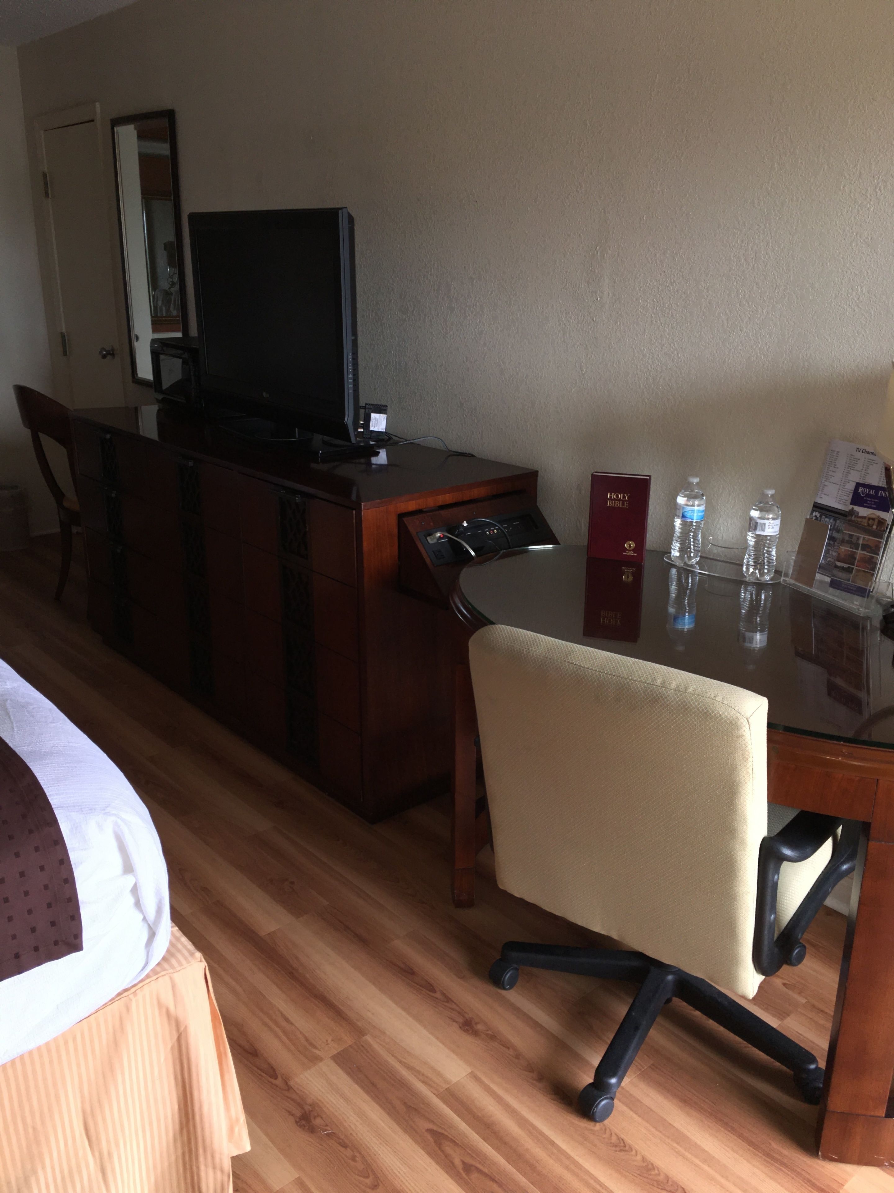 Una habitación de hotel con un escritorio de madera, televisor, espejo, cama y una silla.