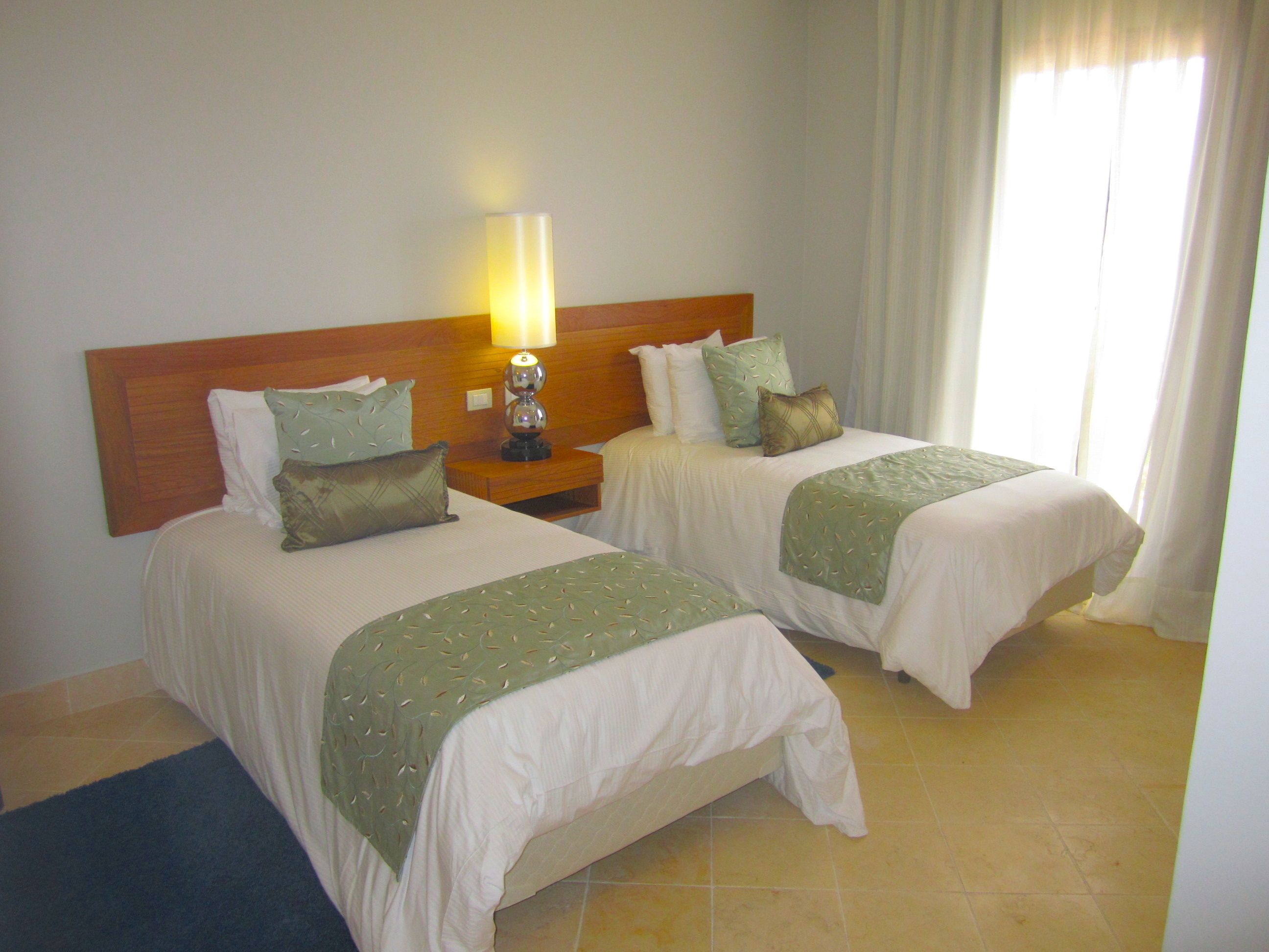 A hotel room with two beds, a nightstand with a lamp, and a window with curtains.