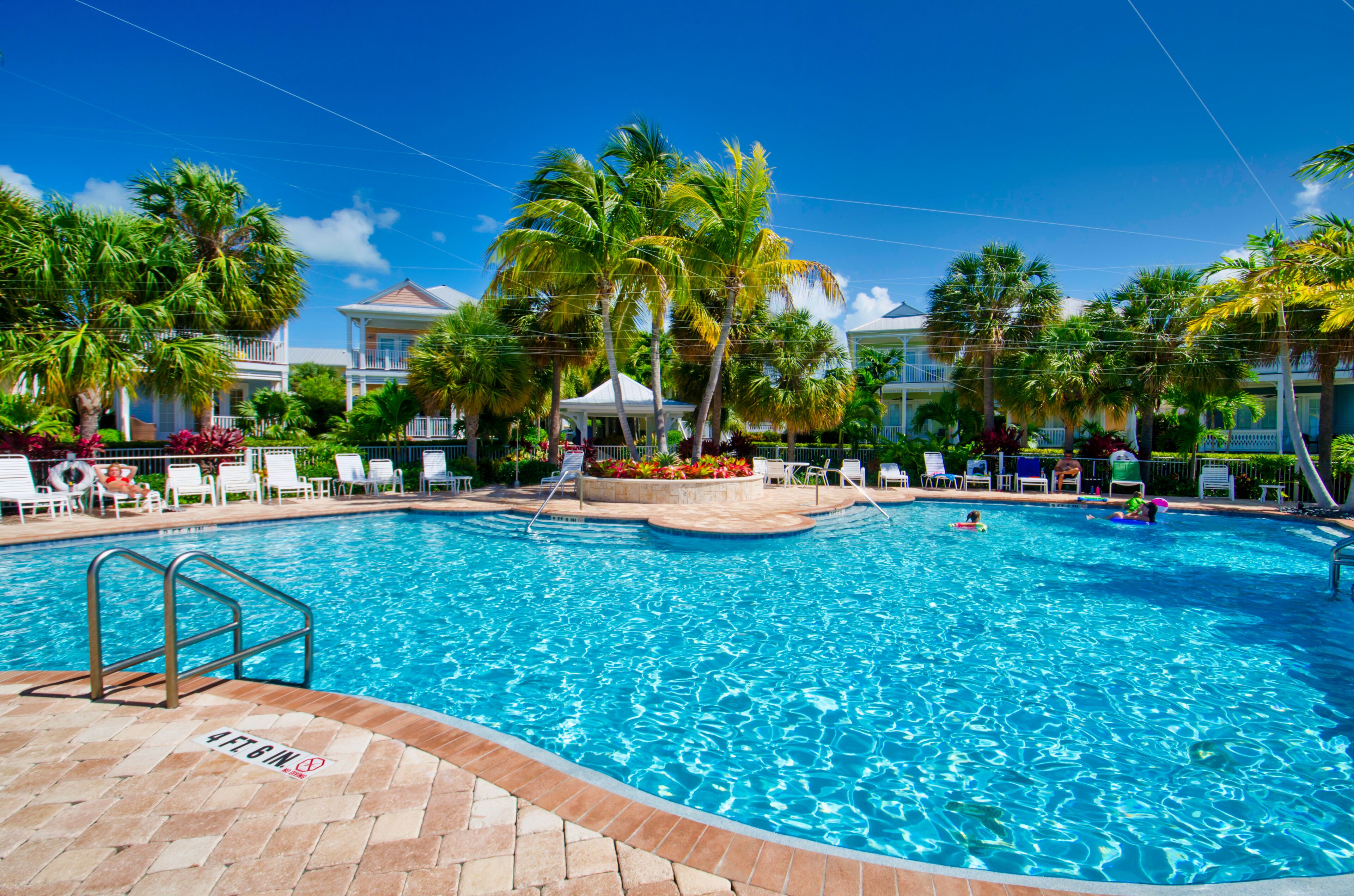 Piscina con sillones de descanso y palmeras.
