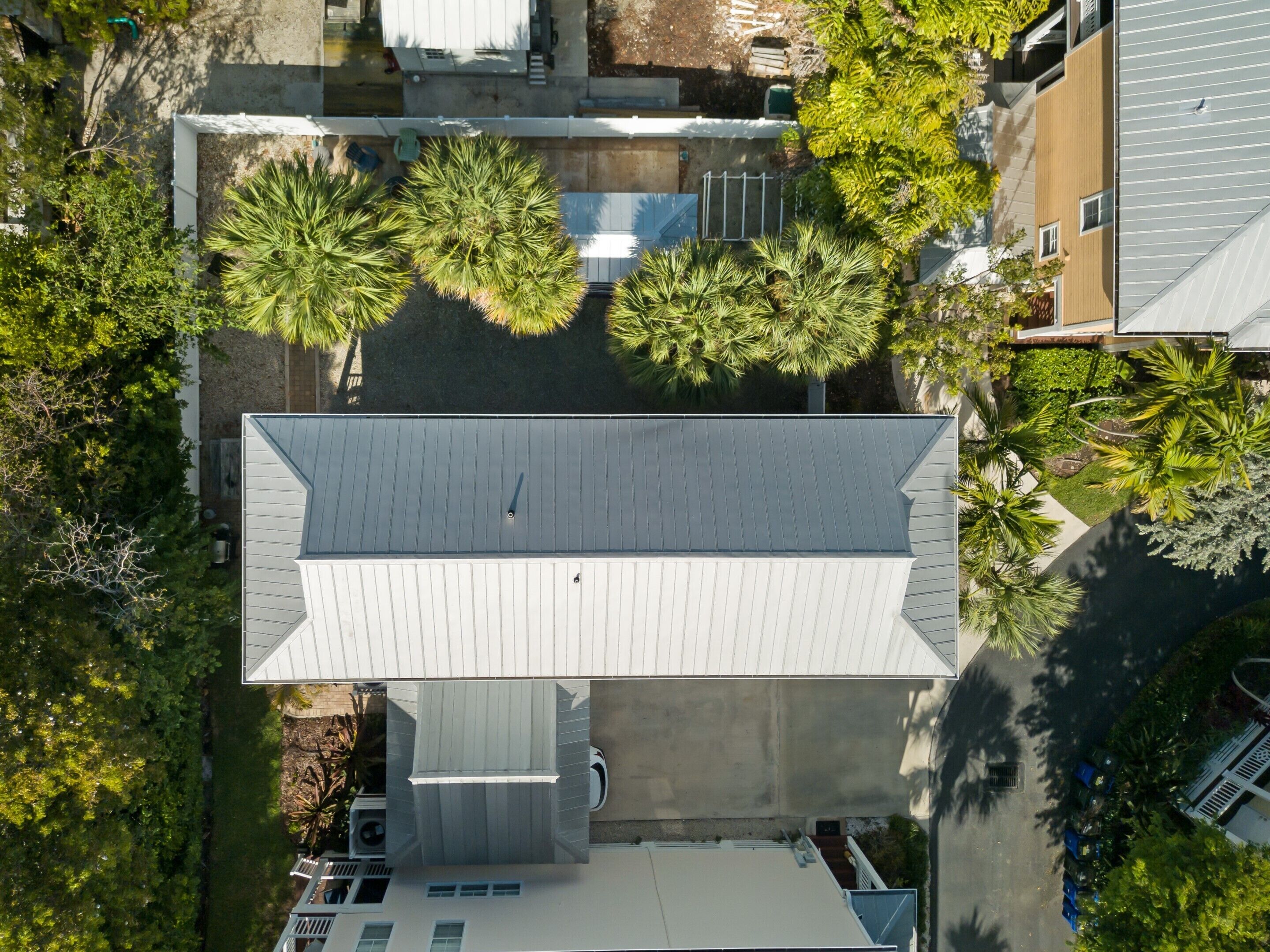 An aerial view of a residential area with a modern house featuring a sloped roof, surrounded by lush greenery and neighboring buildings.