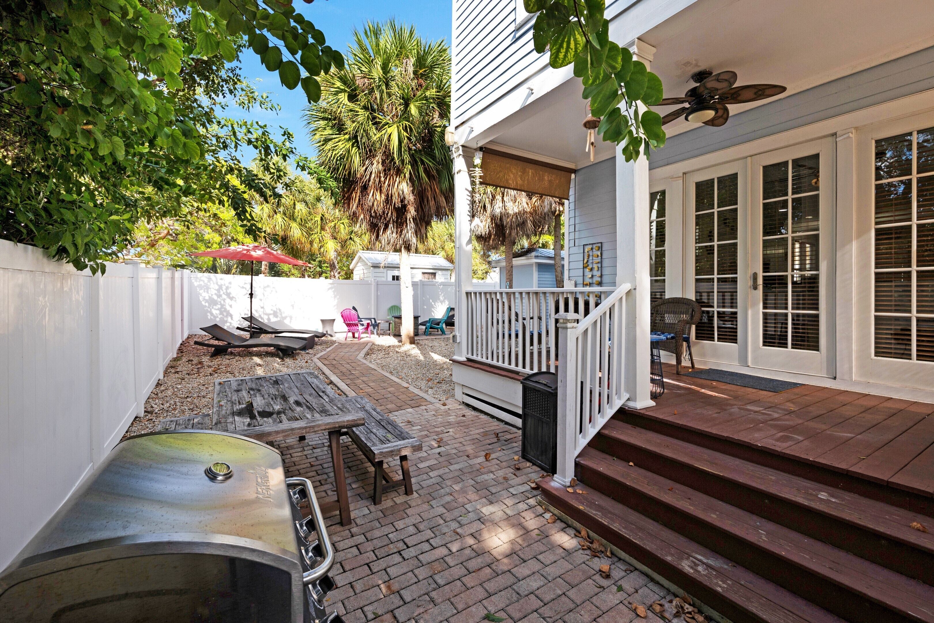 A patio with a grill, outdoor furniture, and a white fence.