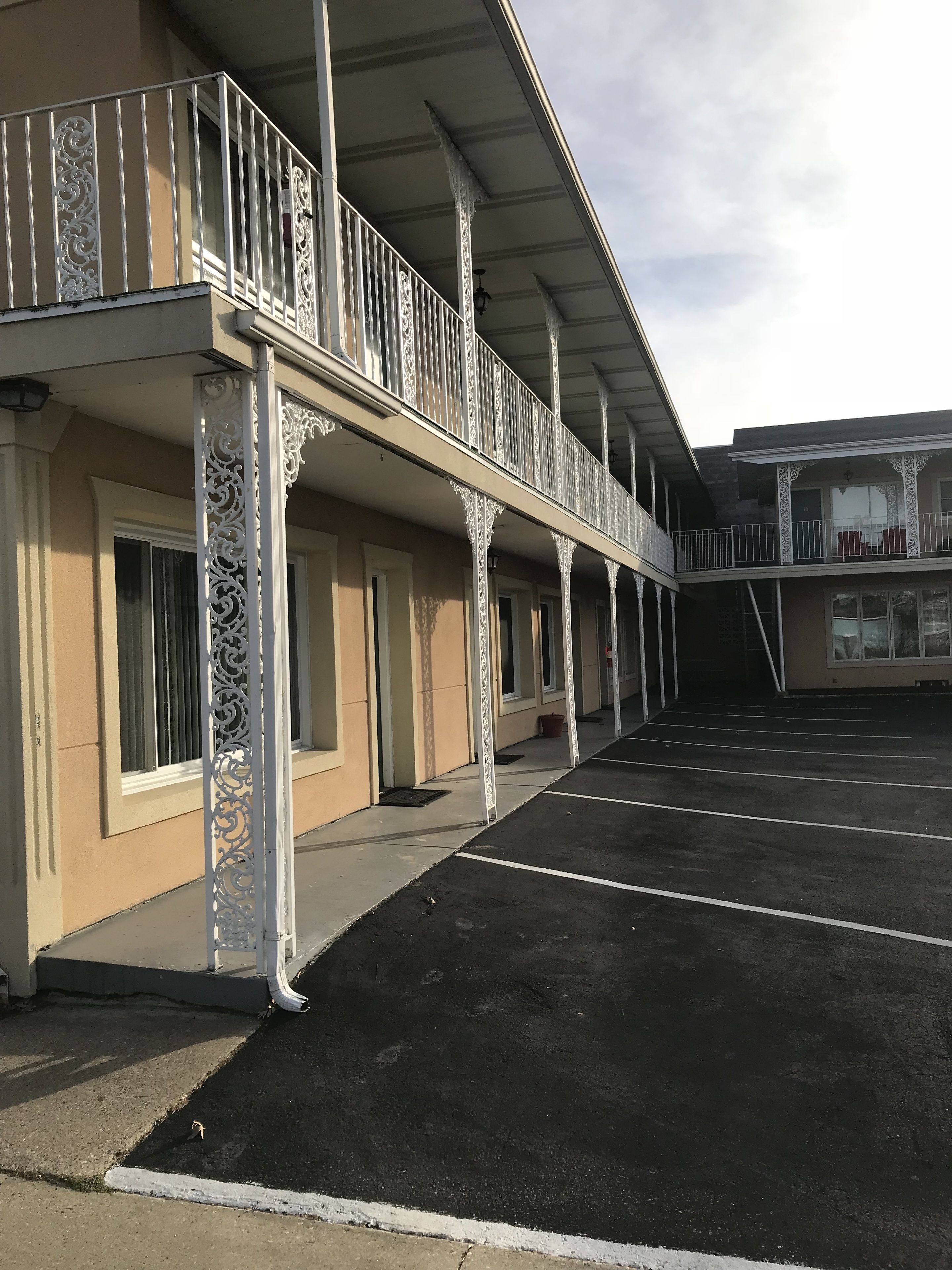 Een gebouw met een overdekt terras, een parkeerplaats en een balkon op de tweede verdieping met versierde balustrades.
