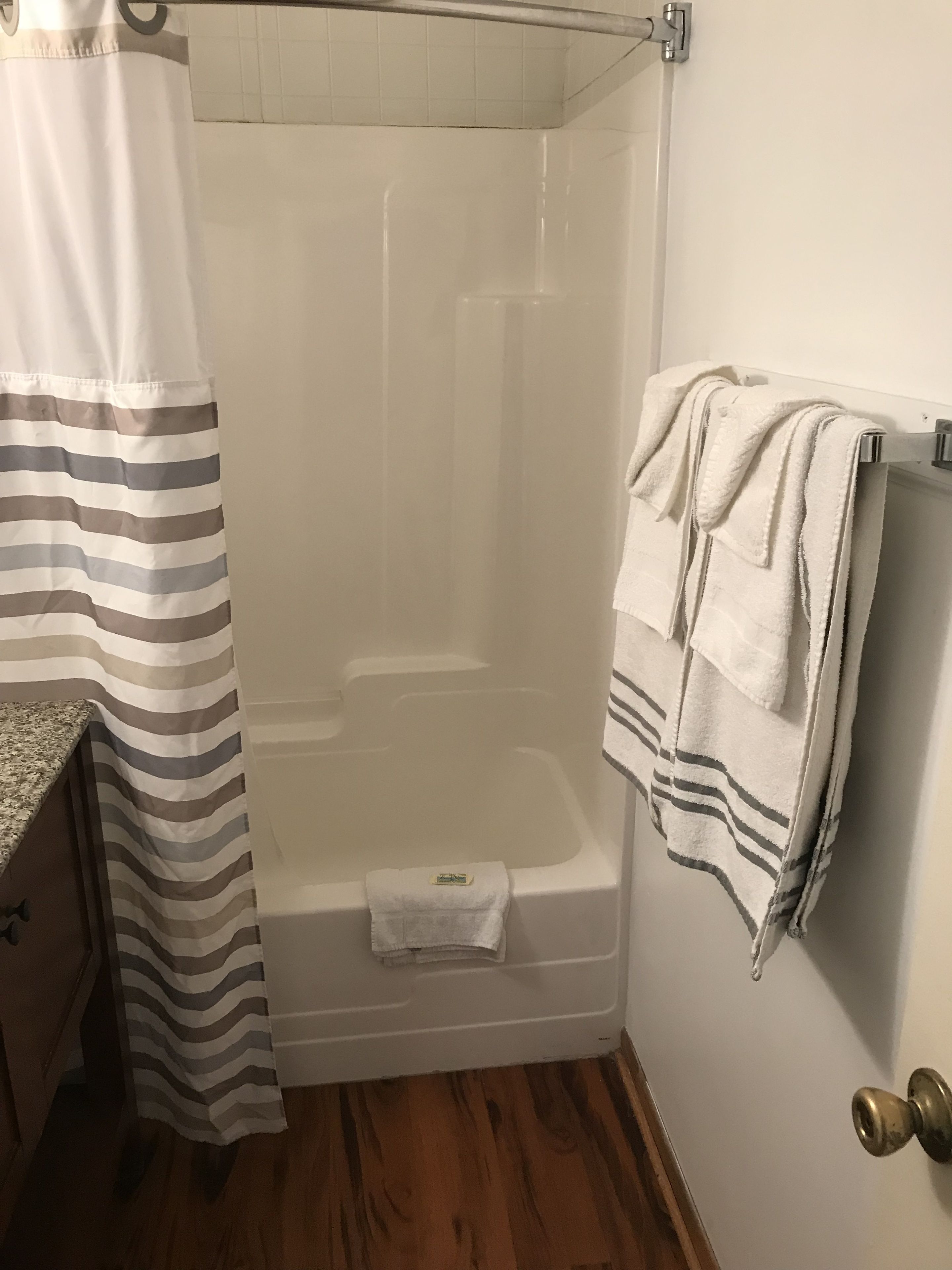 A shower area with a glass door, a towel rack with multiple towels, and a striped shower curtain.