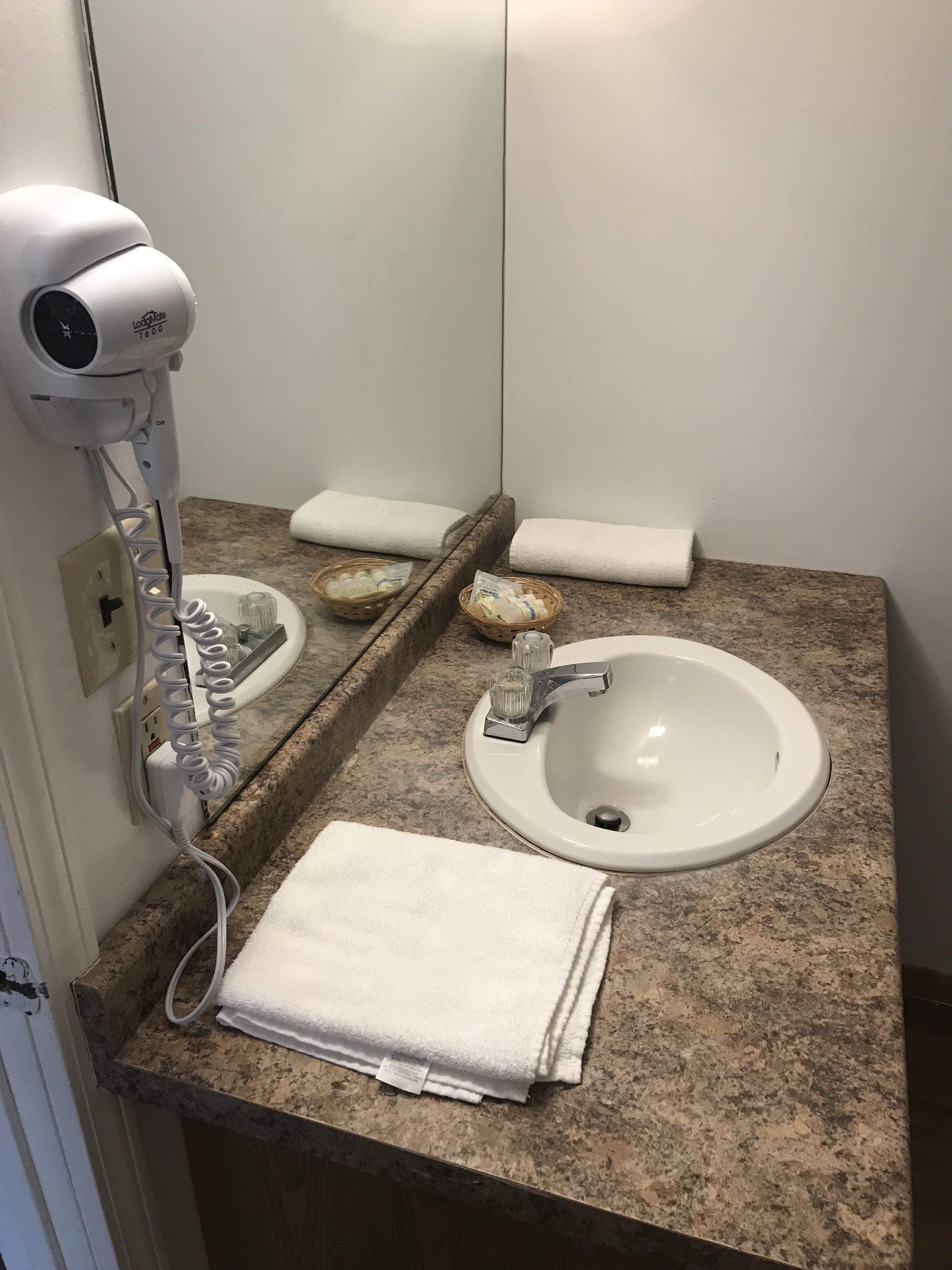 A bathroom with a white sink, a mirror, a hairdryer, and two baskets of toiletries.