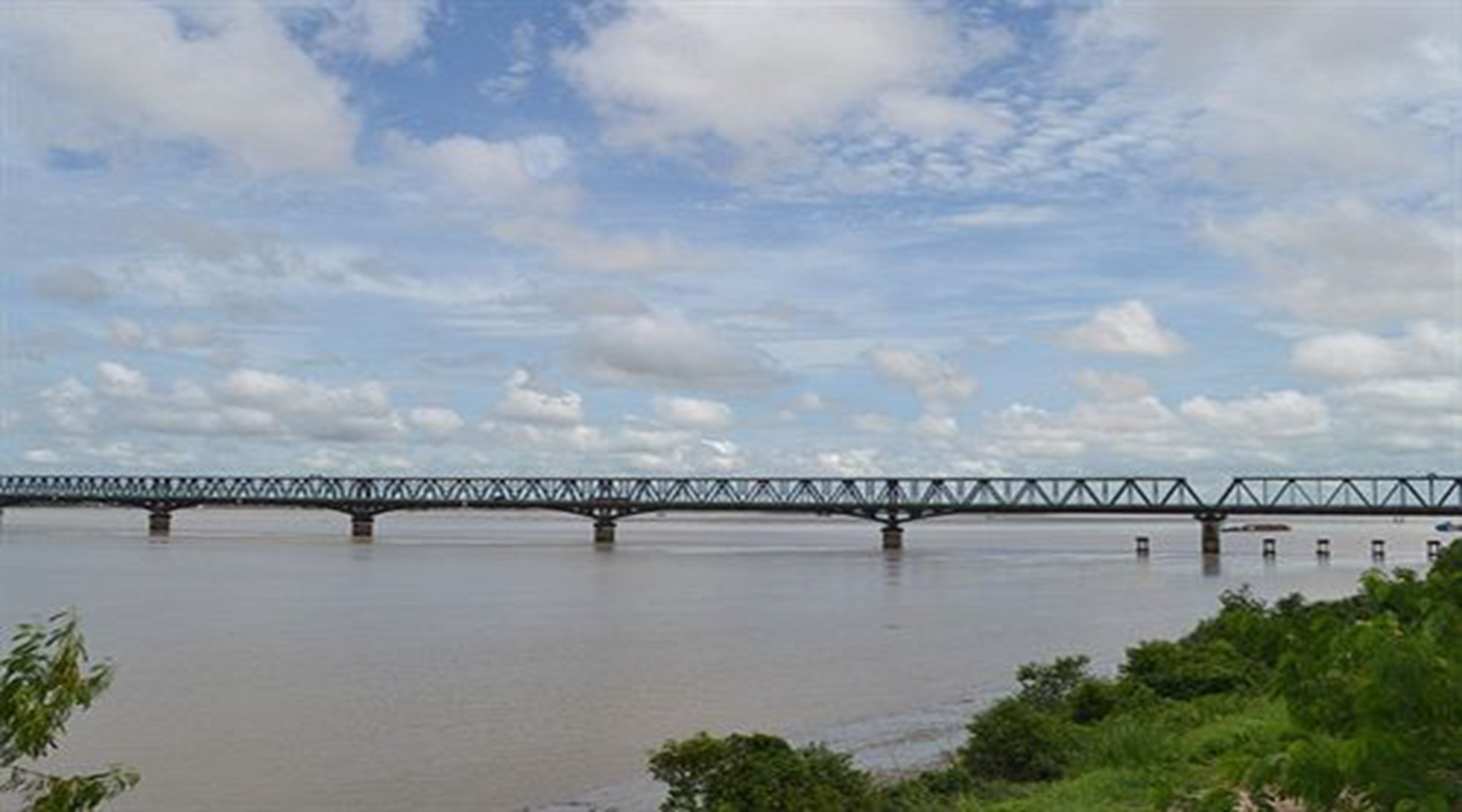 A steel bridge over a calm river with a clear sky.