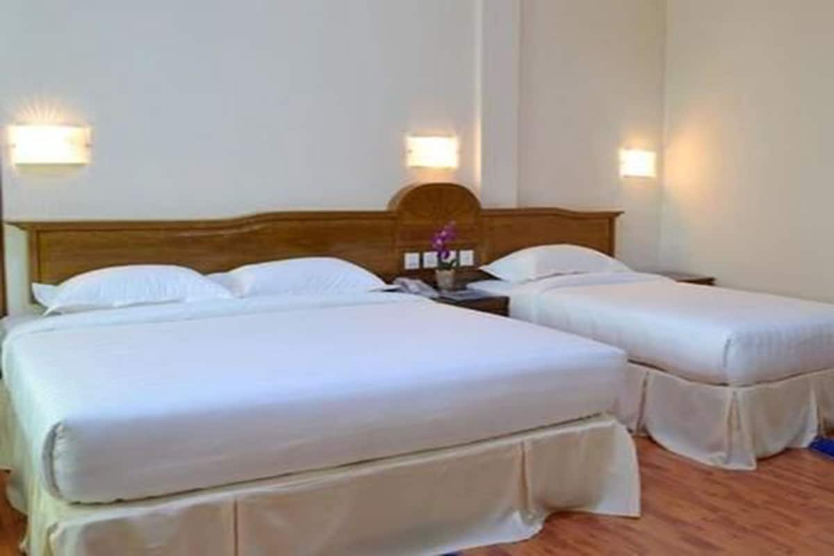 A room with two beds, a wooden headboard, and wall-mounted lights.