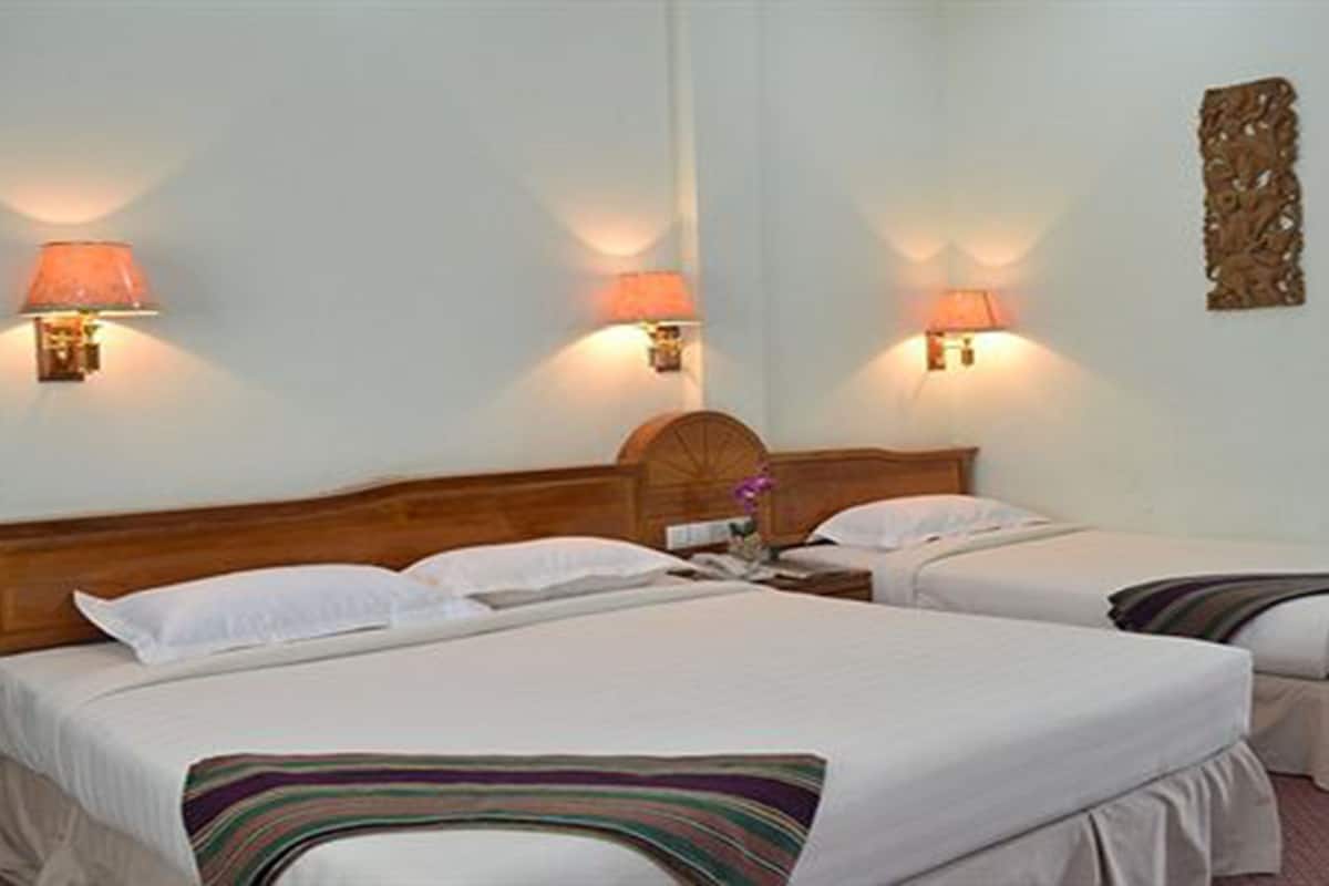 A hotel room with two beds, each with a headboard and bedside lamps.