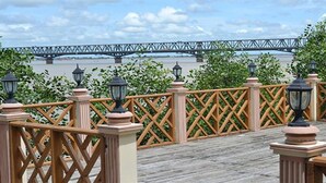 A wooden deck with lattice railings and street lamps, overlooking a river with a bridge in the background. - Excel River View Hotel (Thanlyin)