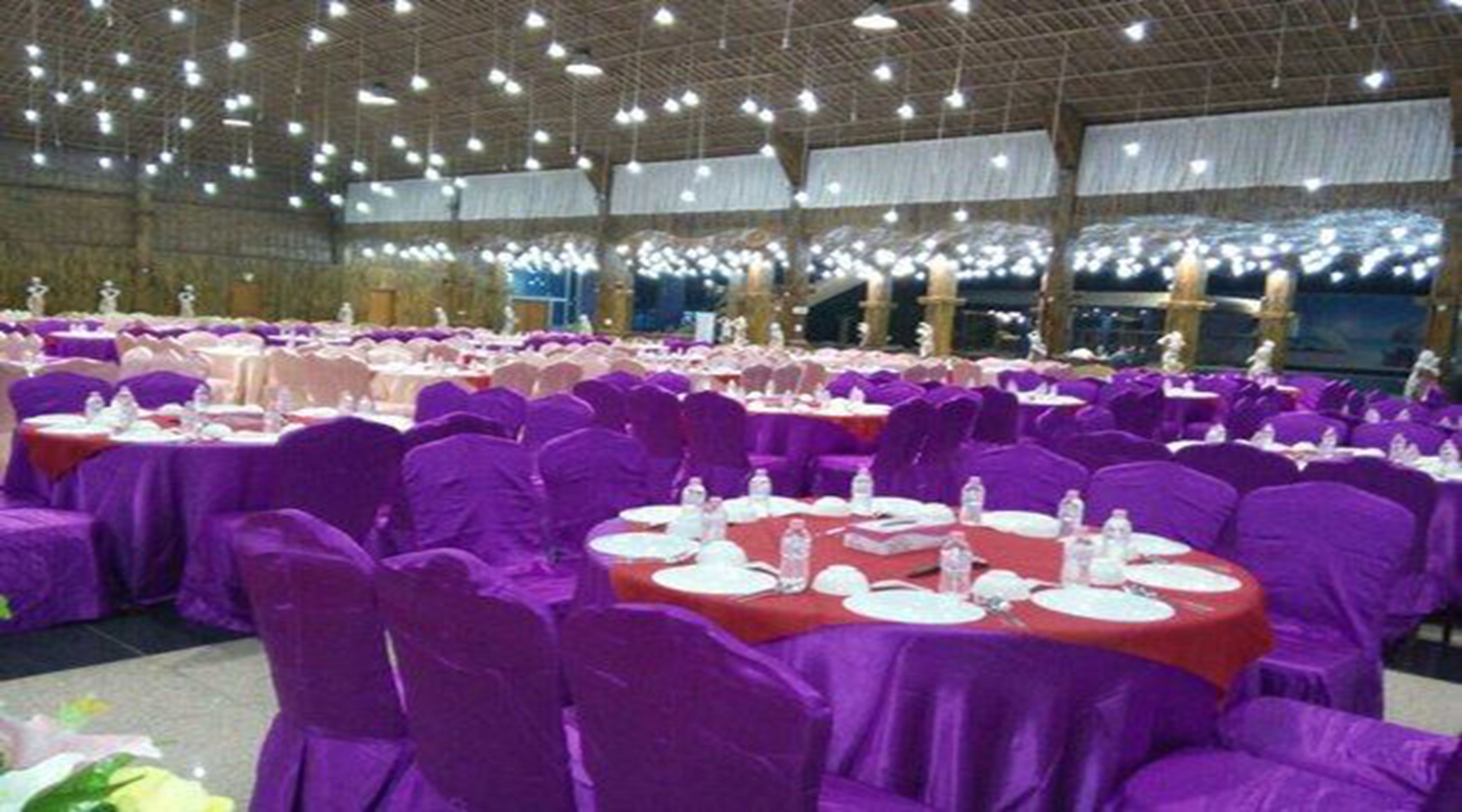 A banquet hall with round tables covered in red tablecloths and purple chairs.
