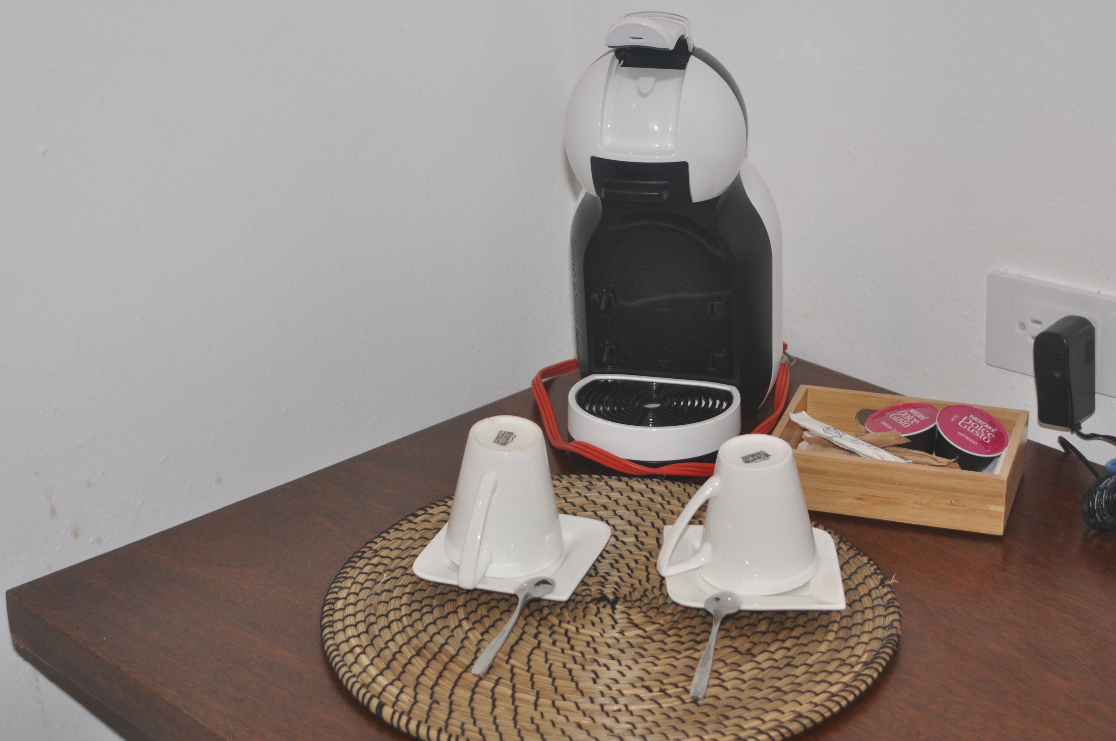 A coffee maker on a table with two white cups and a tray of coffee pods.