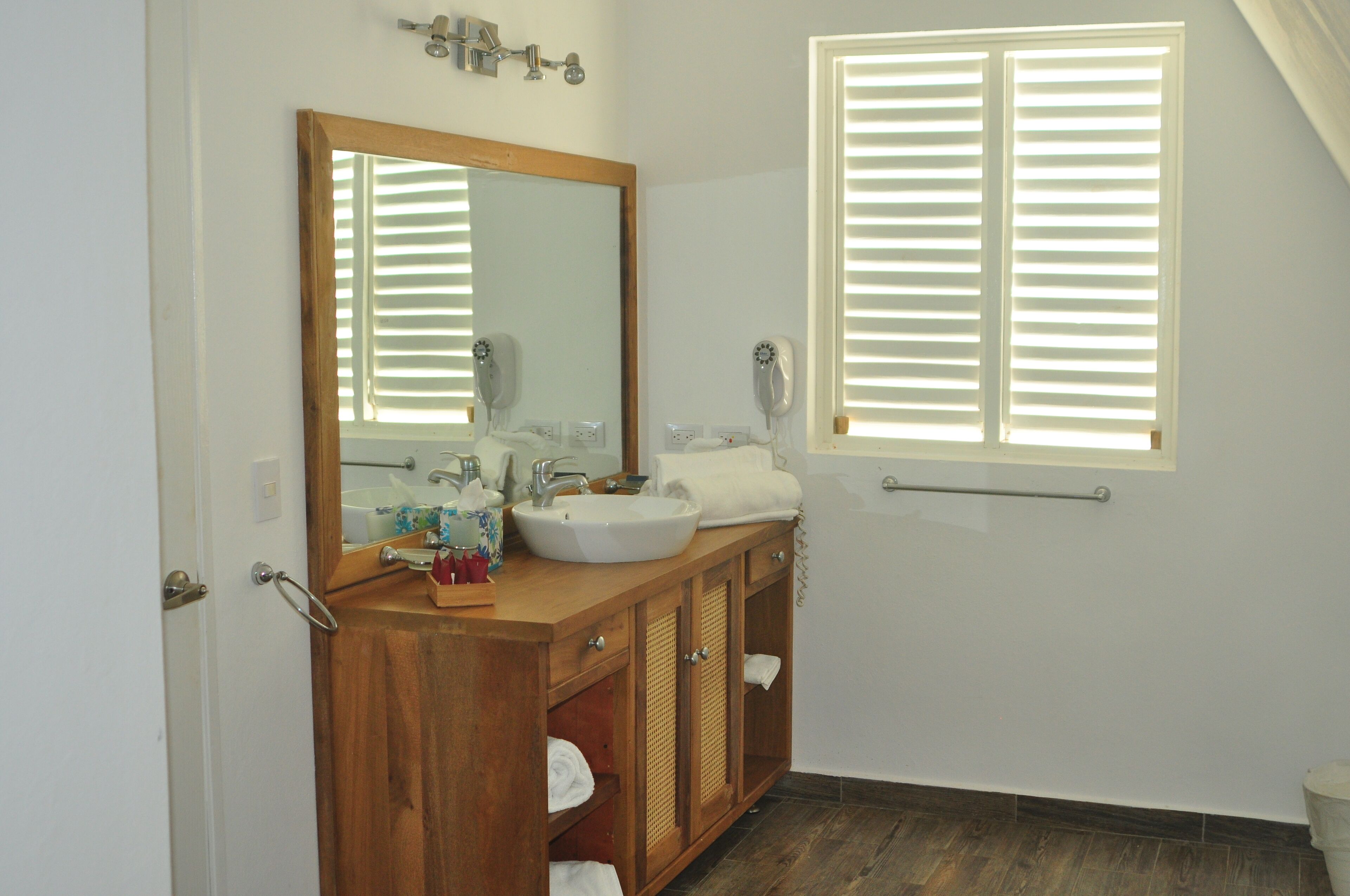 A bathroom with a wooden vanity, a large mirror, a sink, and a window with blinds.
