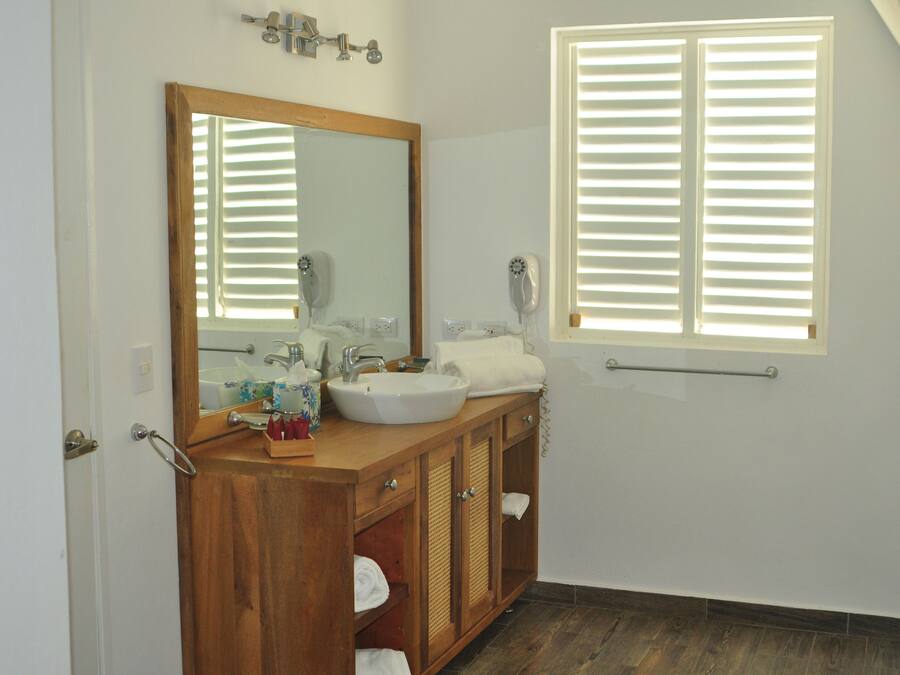 A bathroom with a wooden vanity, a large mirror, a sink, and a window with blinds.