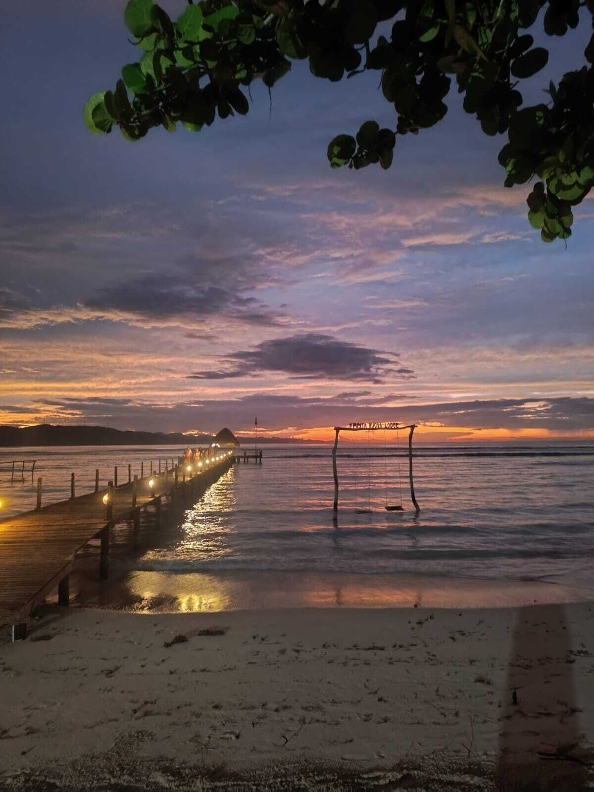 A wooden pier extending into calm waters at sunset with a beach in the foreground.