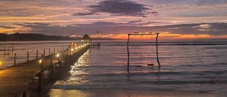 A wooden pier extending into calm waters at sunset with a beach in the foreground.
