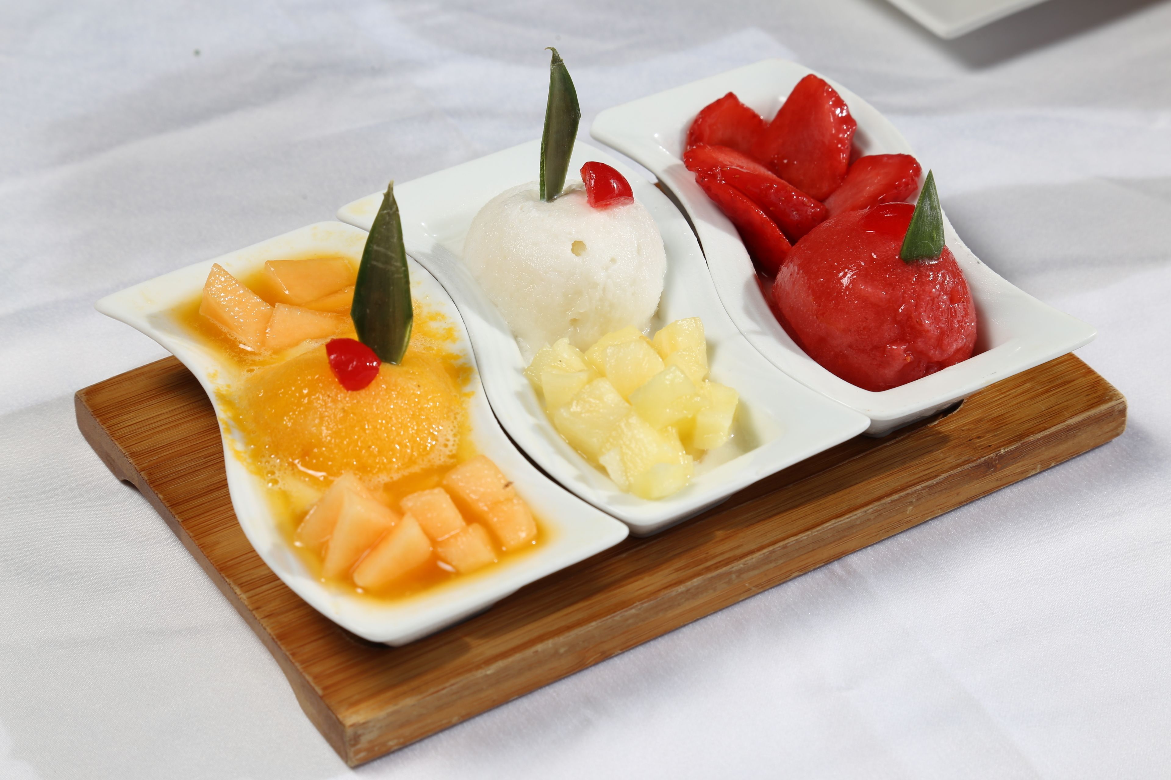 Three white dishes with different fruit toppings on a wooden board.