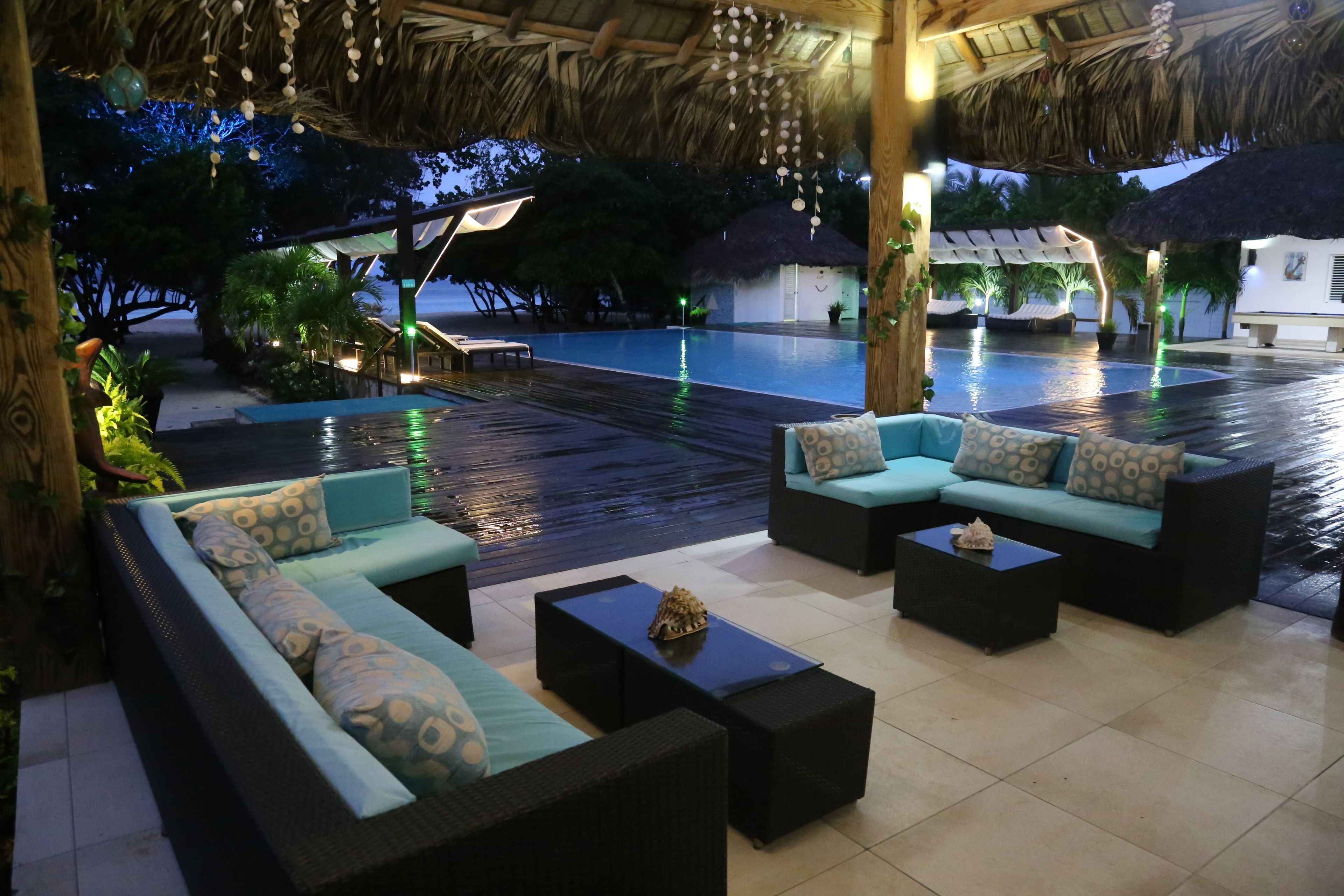 An outdoor lounge area with a pool, thatched roof, and comfortable seating.