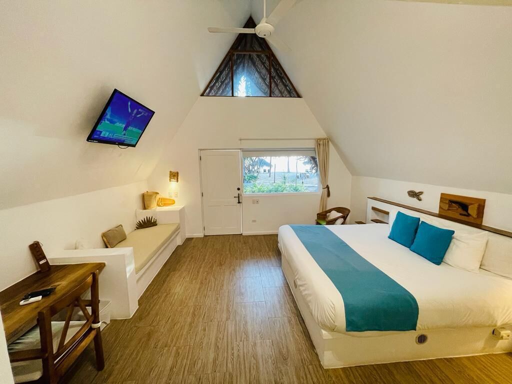 A bedroom with a bed, a desk, a chair, a TV mounted on the wall, and a window.