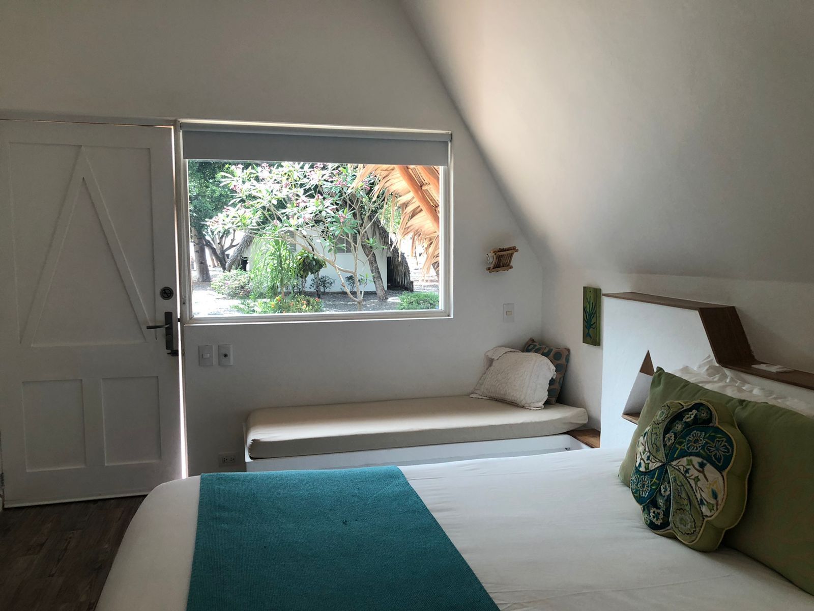 A bedroom with a bed, a window, a bench, and a door.