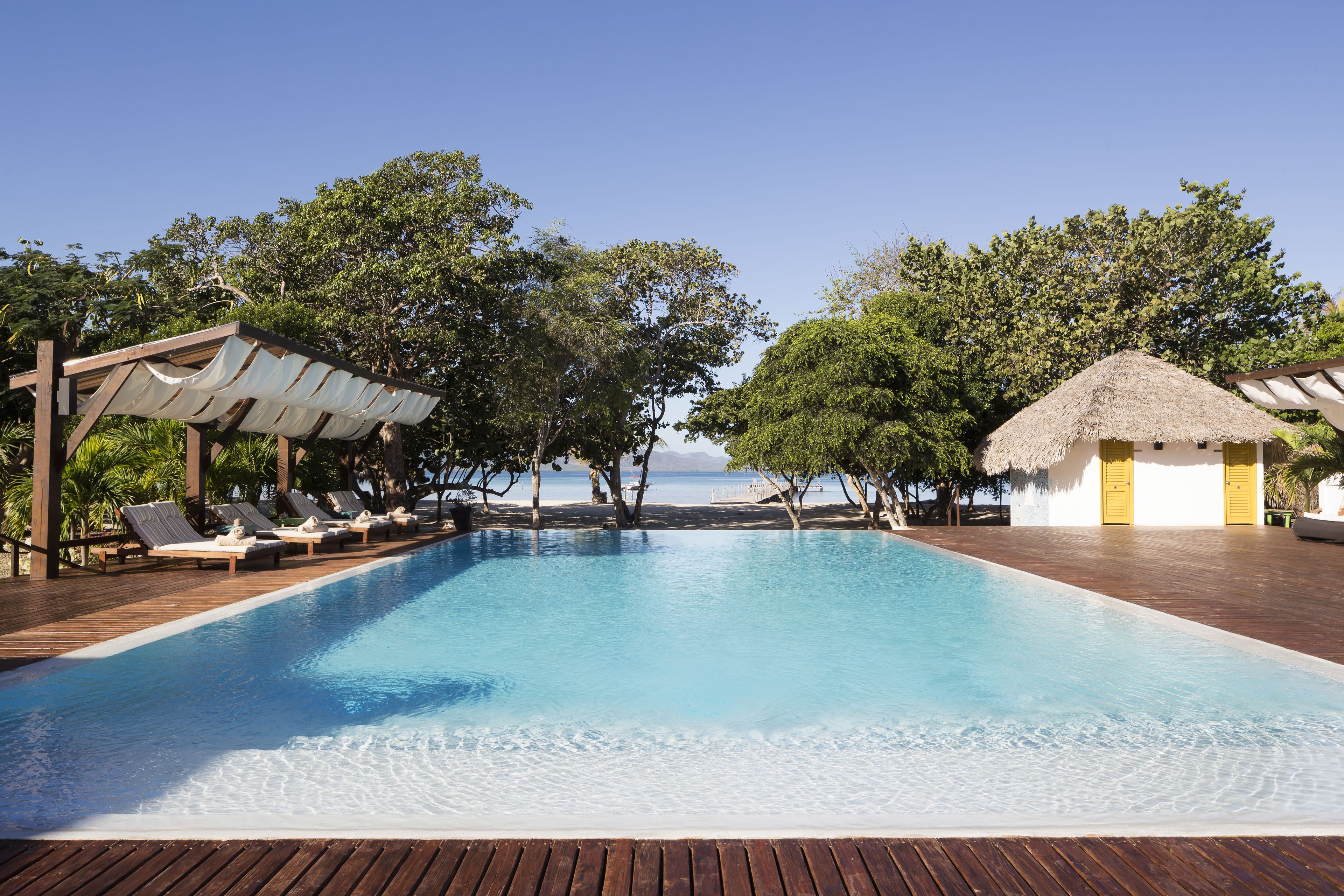 Piscina com espreguiçadeiras e uma estrutura coberta de palha.