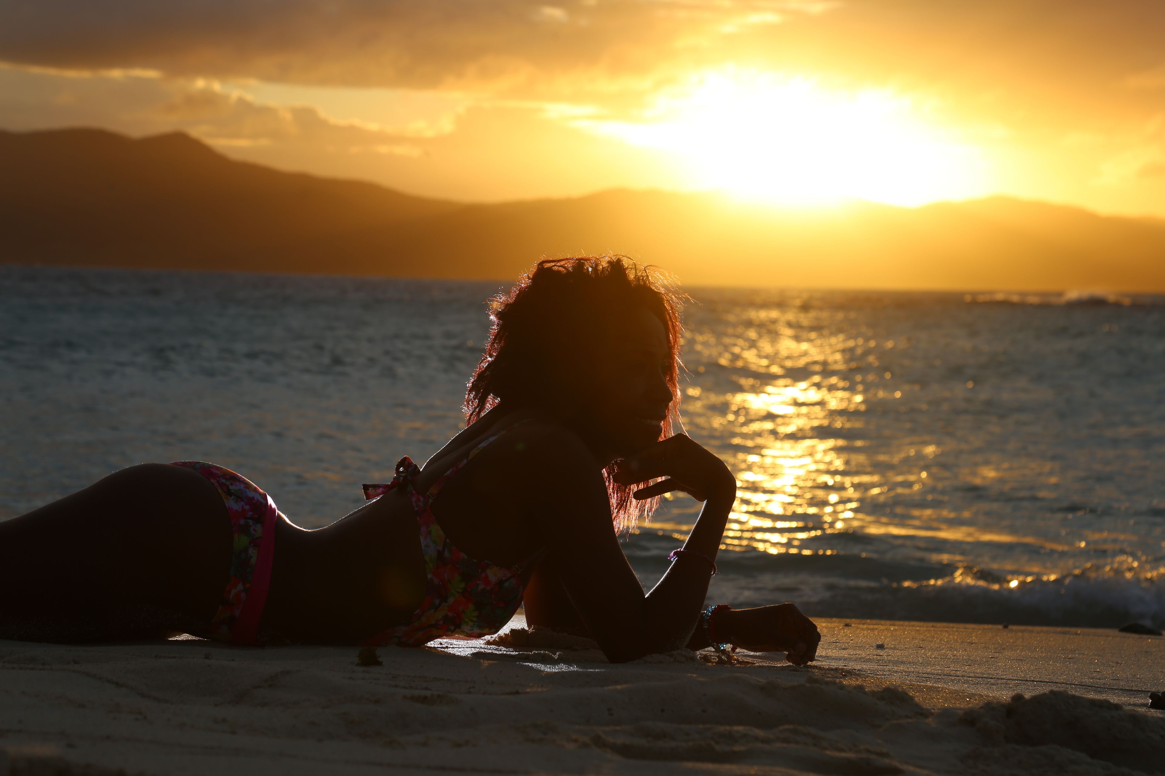 Une personne allongée sur une plage, avec un coucher de soleil en arrière-plan.