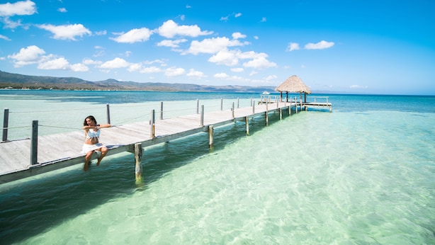A clear view of a pier extending into turquoise waters with a thatched-roof structure at the end.