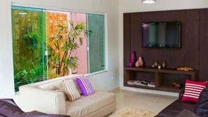 Una sala de estar moderna con un sofá, un televisor montado en la pared y un ventanal con vistas al follaje.