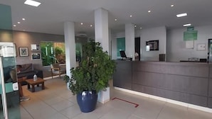 Un vestíbulo amplio con mostrador de recepción, zona de estar y una planta grande en maceta.