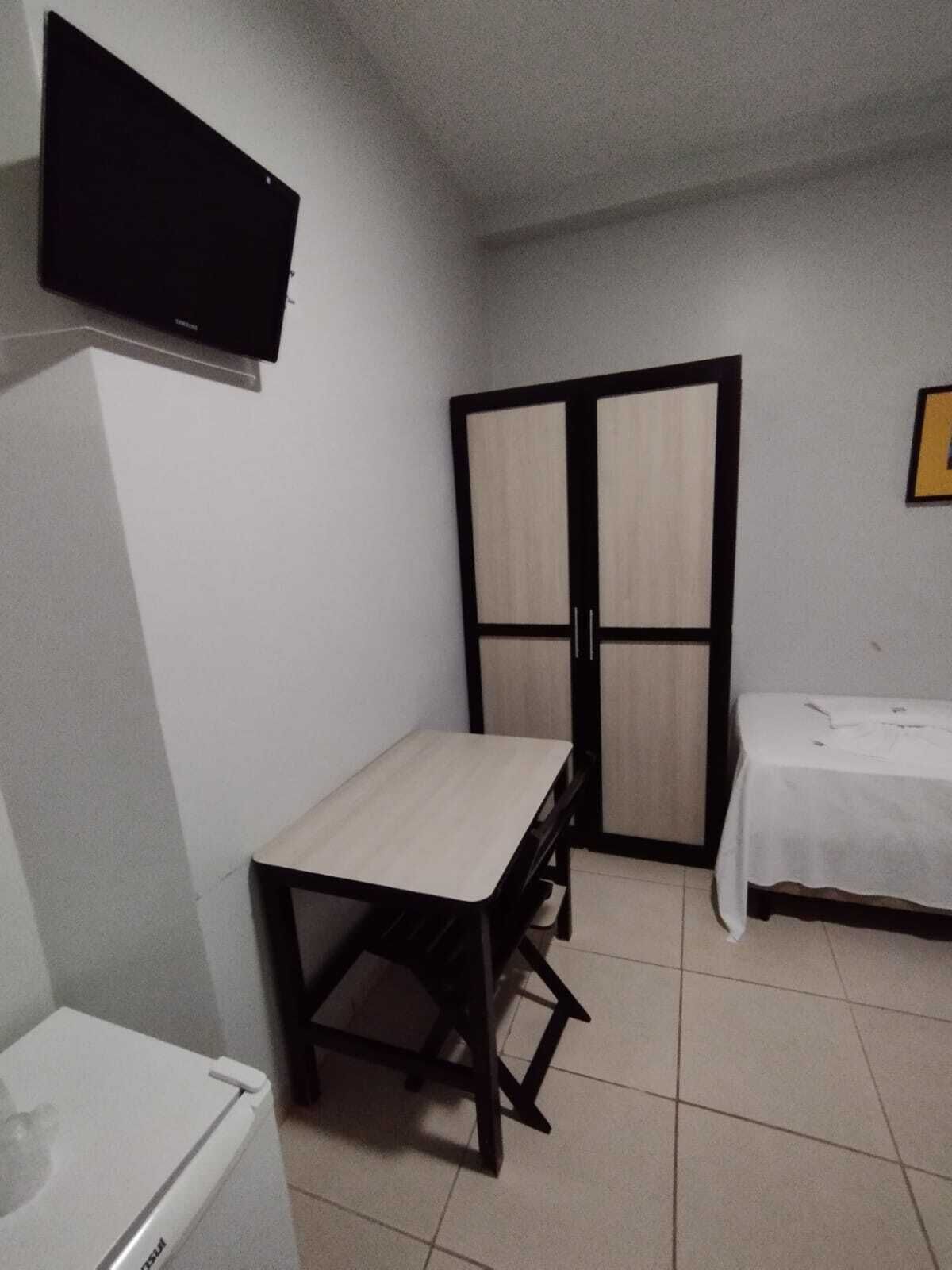 Una habitación pequeña y sencilla con escritorio, cama y armario.