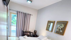 Habitación de hotel con cama, televisor montado en la pared, escritorio con silla y dos cuadros enmarcados.