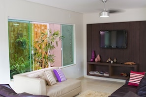 Una sala de estar moderna con un sofá, un televisor montado en la pared y un ventanal con vistas a zonas verdes.