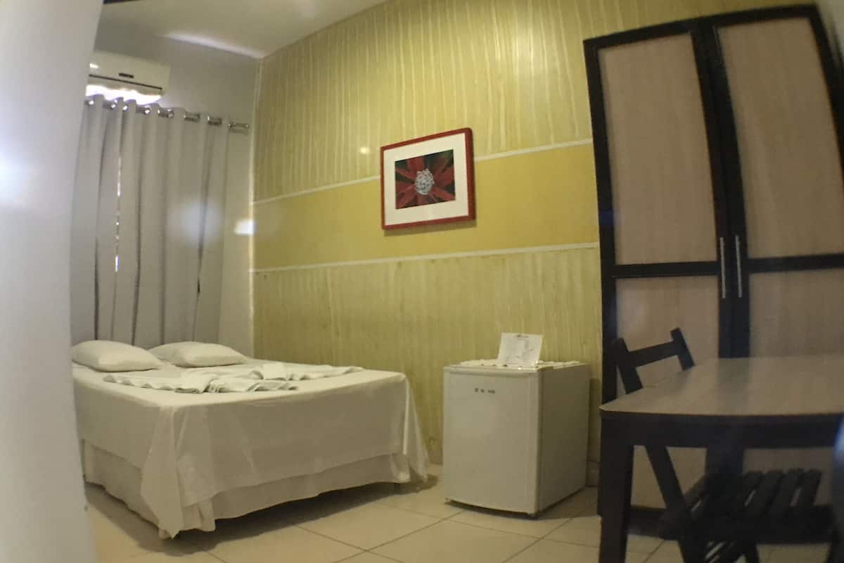 A hotel room with a bed, a small table, a chair, a refrigerator, and a picture on the wall.
