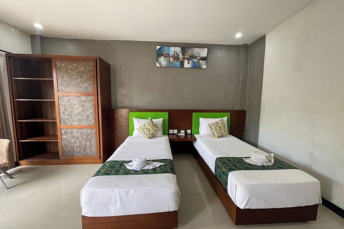 A hotel room with two single beds, a wardrobe, a small table, and a wall-mounted artwork.