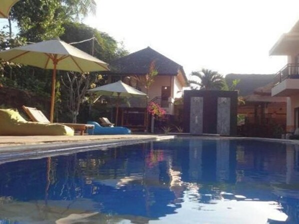 A swimming pool with lounge chairs and umbrellas, surrounded by buildings and greenery. - Melati Resort & Hotel Kuta Lombok (Kuta)