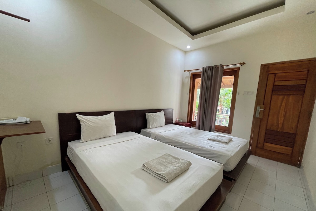 A hotel room with two beds, a small desk, and a window with curtains.