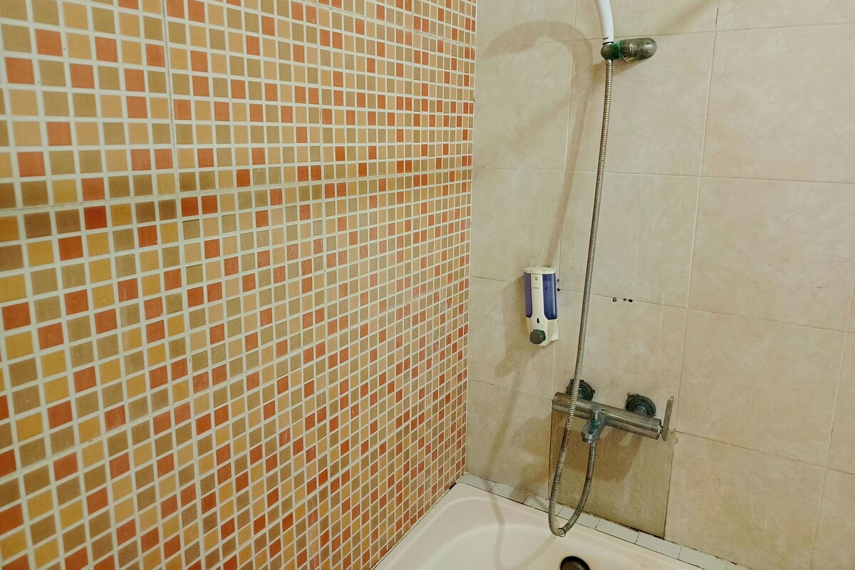 A bathroom with a tiled floor, a shower with a handheld showerhead, and a wall-mounted soap dispenser.