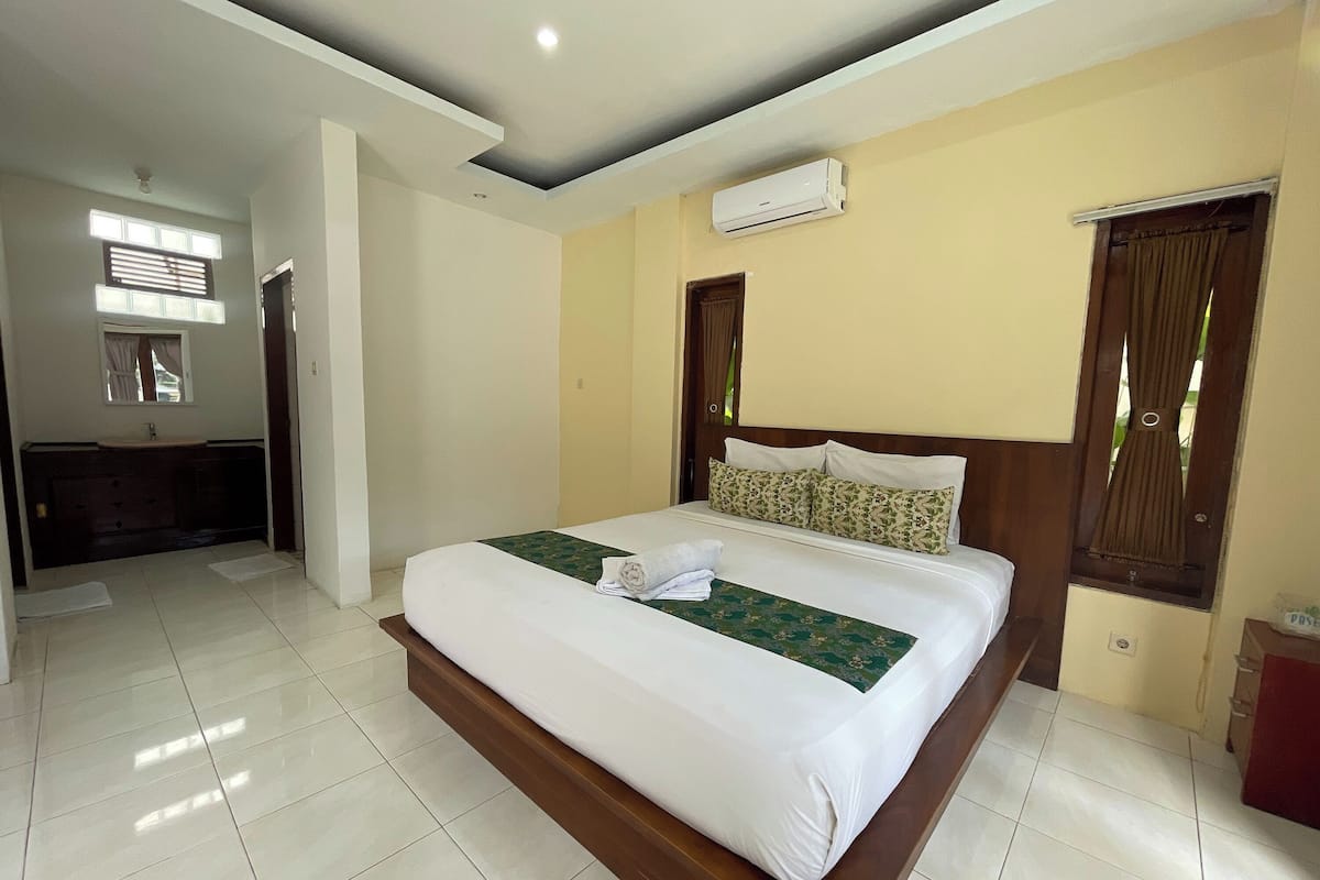 A hotel room with a large bed, a bathroom with a sink, and an air conditioning unit on the wall.