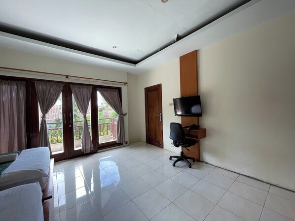 Habitación de hotel con cama, escritorio, silla, televisor y balcón con cortinas.