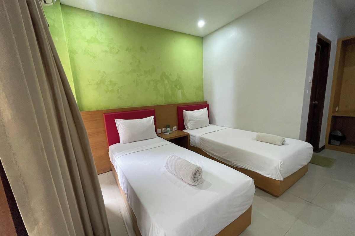 A hotel room with two beds, a green wall, and a wooden headboard.