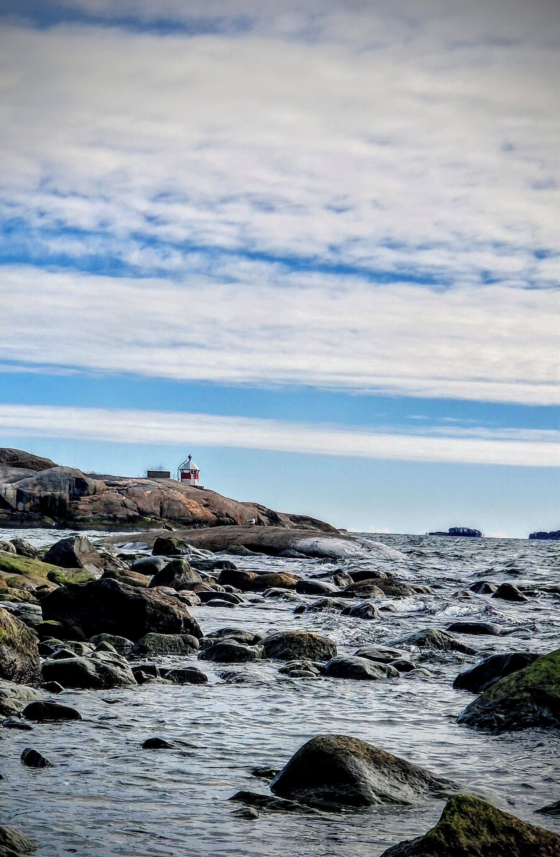 A rocky shoreline with a lighthouse and waves.