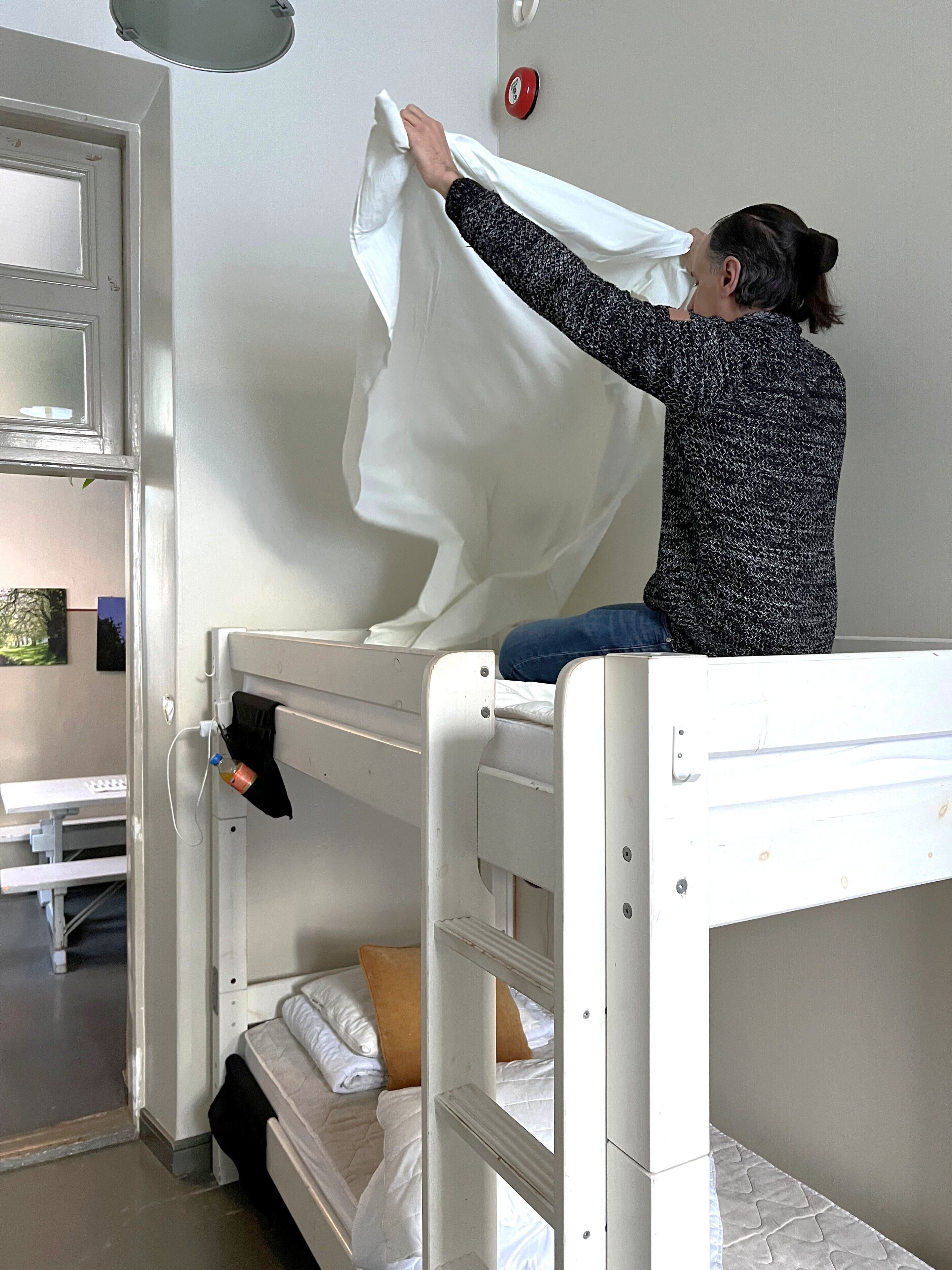 A bunk bed with a person adjusting a white sheet.